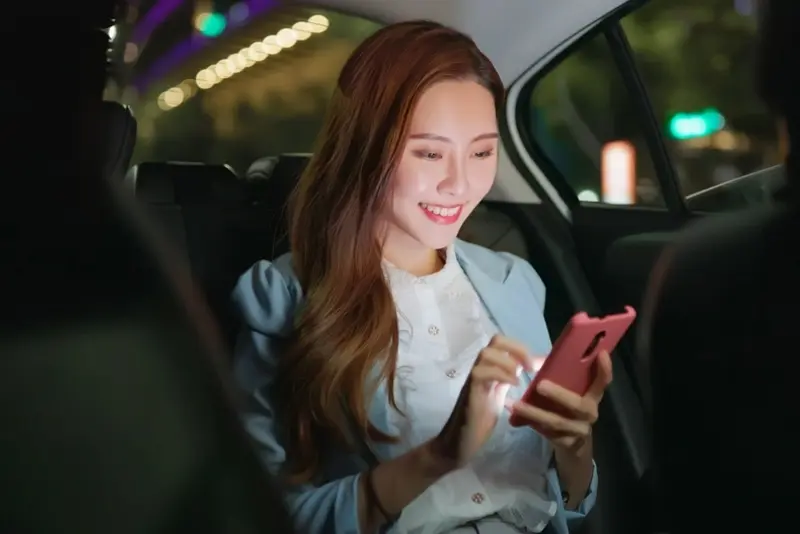 A young woman, looking happy and content, uses her mobile phone while using luxury transportation services, symbolizing private chauffeur services in Austin.